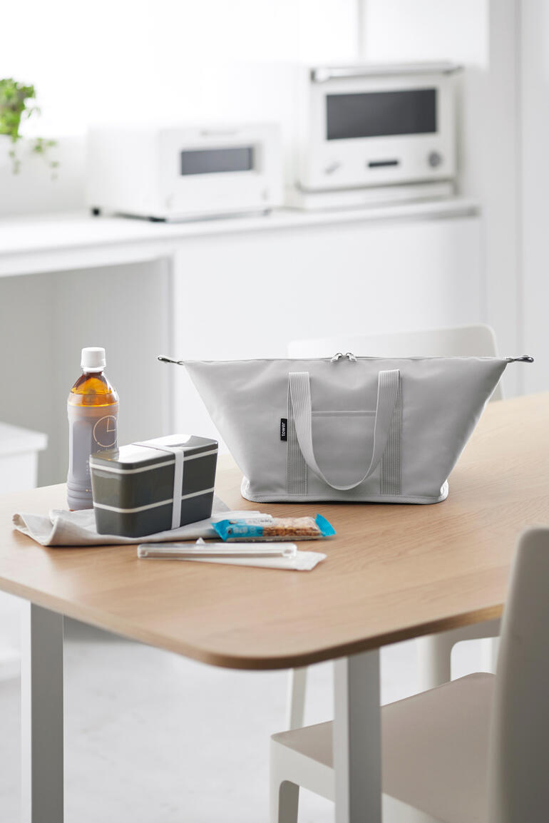 Sac isotherme Vario gris clair sur une table, entouré de collations et de boissons.