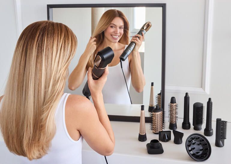 Femme coiffe ses cheveux avec un styliste 12-en-1 devant un miroir.
