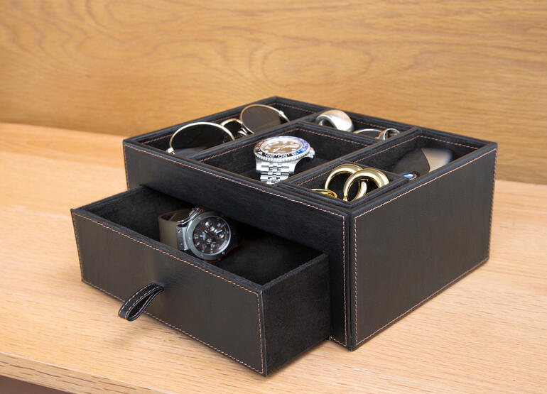 Boîte de rangement noire en cuir contenant divers accessoires comme des montres et des lunettes.