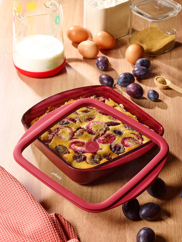 Plat à four rouge avec couvercle, rempli d'un plat aux fruits sur une table.