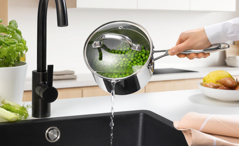 Casserole à long manche avec couvercle, de l'eau est versée dans l'évier.