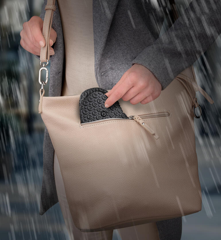 Une personne sort un couvre-chaussures en silicone noir de son sac sous la pluie.