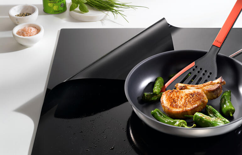 Poêle avec courgettes et un côtelettte sur une protection de plaque à induction