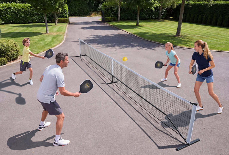 Une famille joue au pickleball en plein air, avec un filet et des balles.