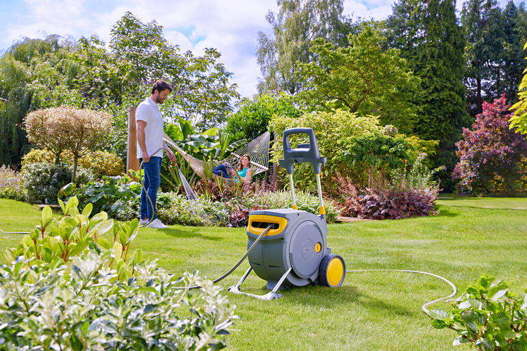Homme arrosant avec un tuyau d'un enrouleur de tuyau fermé