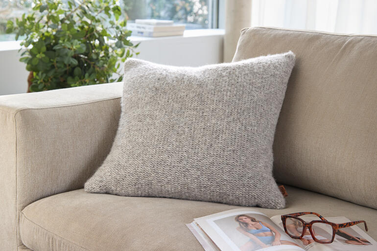 Coussin en alpaga-lin sur un canapé clair avec des lunettes et un magazine.
