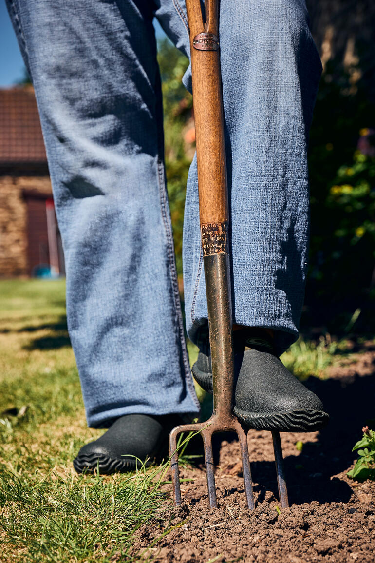 Personne debout avec une pelle de jardin, portant des chaussures de jardin Airmesh noires.