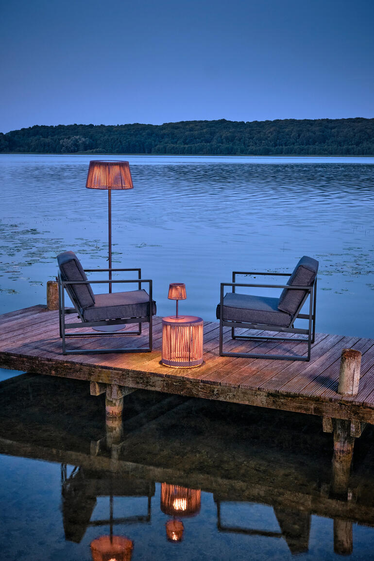 Table de jardin avec éclairage LED au bord de l'eau, entourée de chaises.