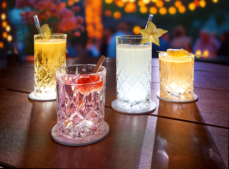 Quatre verres illuminés sur une table avec des sous-verres LED, idéaux pour une atmosphère festive.