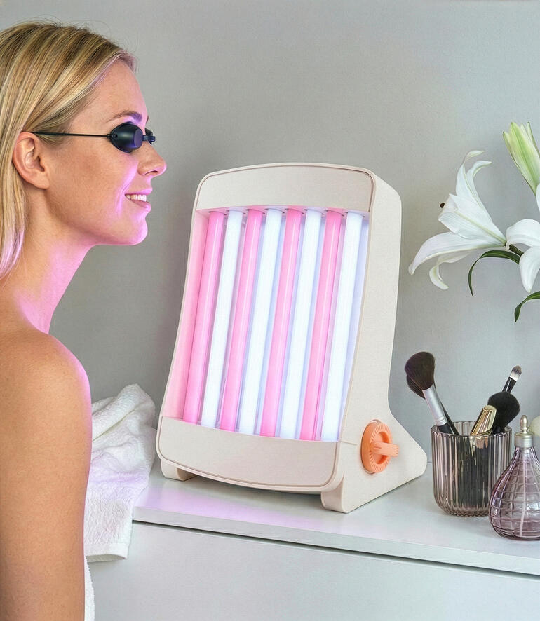 Bronzer facial avec des lampes roses et bleues, placé sur une table à côté de produits cosmétiques.
