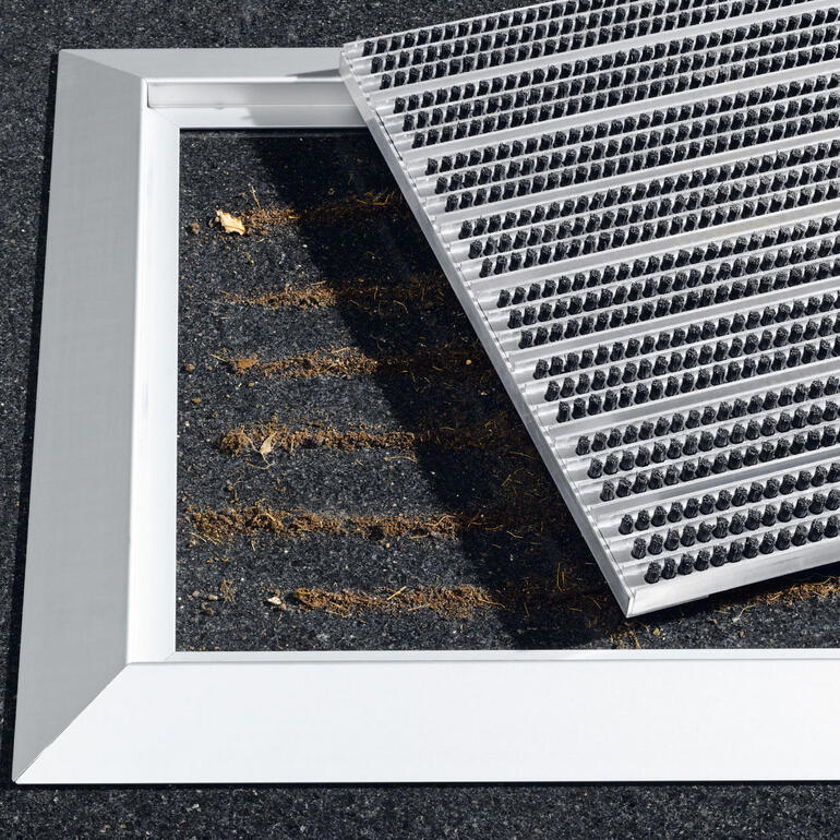 Pour le nettoyage, il vous suffit de soulever la grille à brosses et d’aspirer ou de balayer tout simplement les accumulations de saleté. Tapis d'entrée en aluminium avec platine amovible sur un sol.