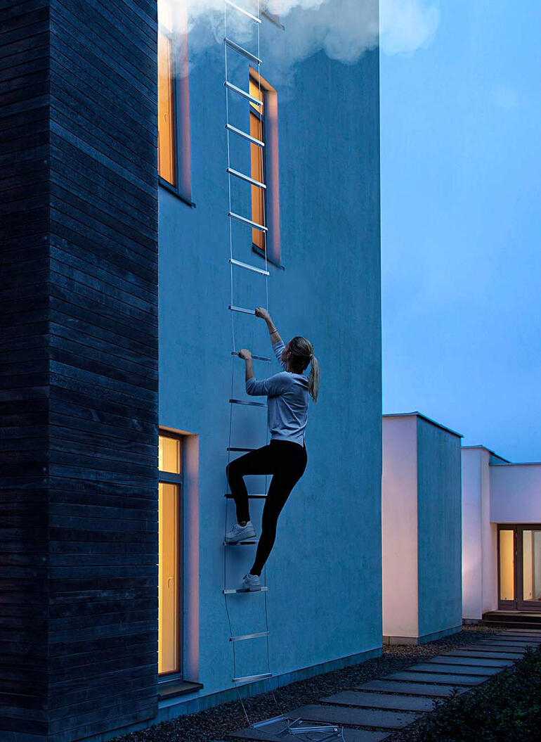 Une femme grimpe sur une échelle de secours le long du mur.