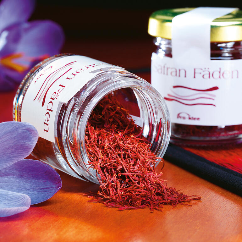 Fils de safran iraniens dans un pot, entourés de plantes fleuries.