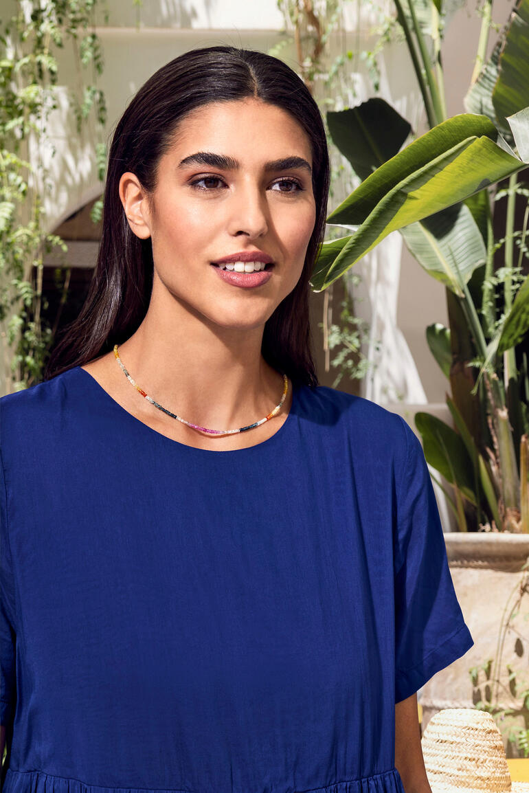 Collier de saphirs Femme avec un collier de saphirs, souriante en plein air, entourée de plantes.