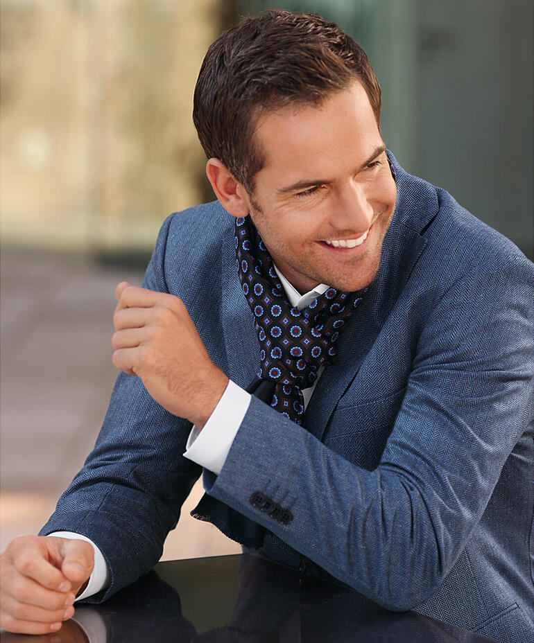 Homme souriant dans une veste en soie à chevrons bleue avec un foulard coloré.