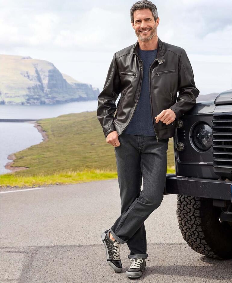 Homme en cuir noir devant un véhicule tout terrain dans la nature.