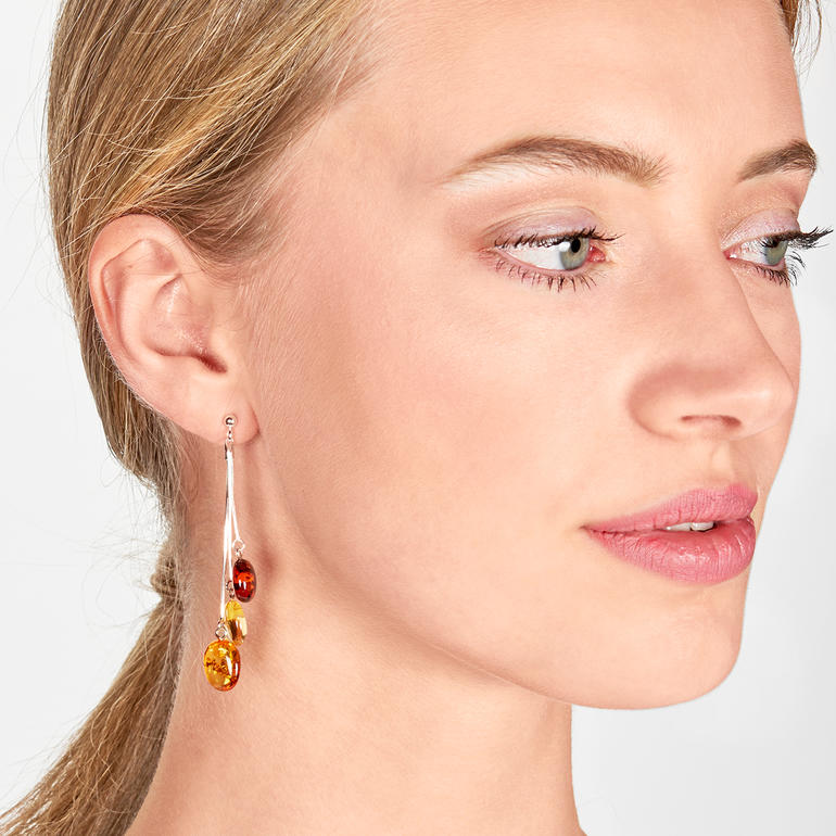 Boucles d'oreilles en ambre suspendues à l'oreille d'une femme.