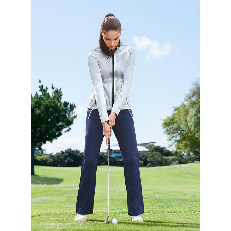 Femme en tenue de golf avec une veste argentée et un pantalon bleu sur le parcours