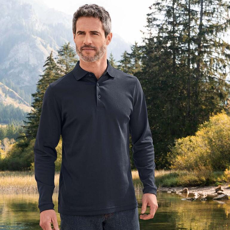 Homme en polo en interlock Pima noir, debout dans un environnement naturel avec des montagnes en arrière-plan.