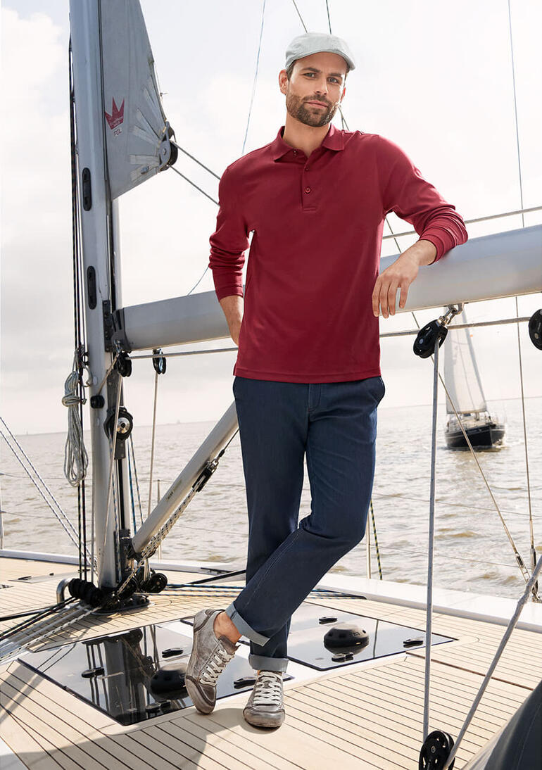 Jean en soie Homme en polo Pima interlock rouge debout sur un bateau, souriant.