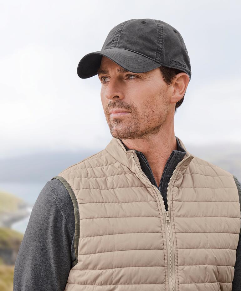 Homme en casquette Stetson et gilet à l'extérieur, avec vue sur un paysage.