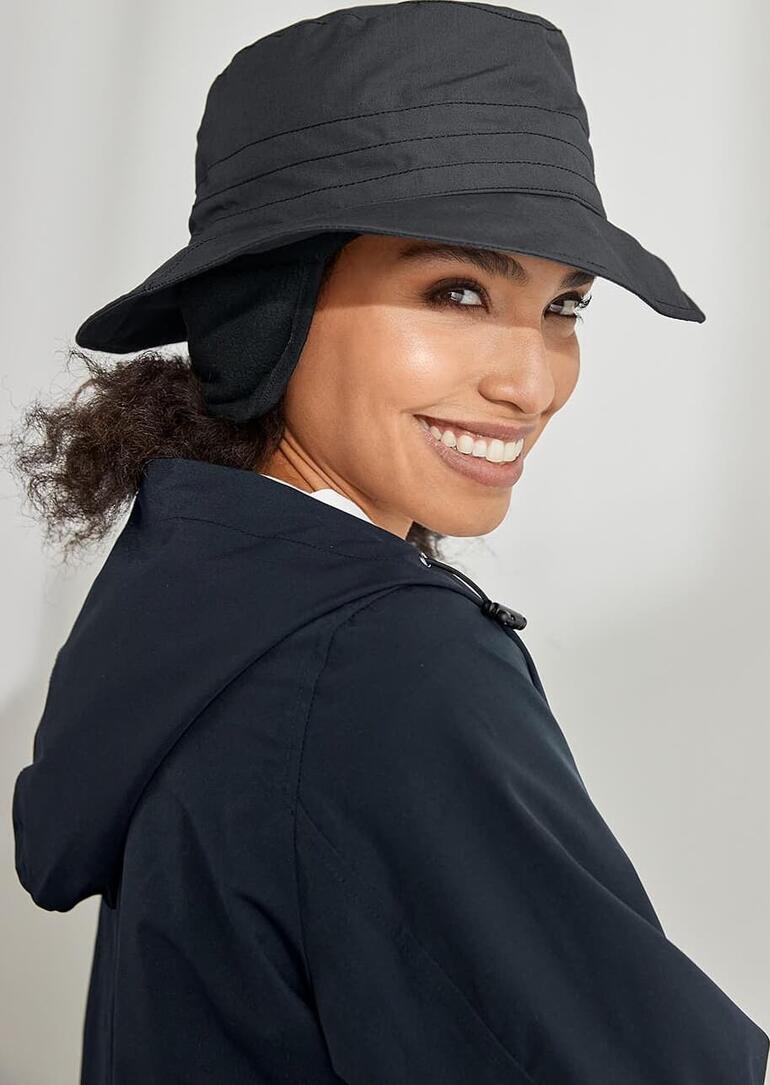 Chapeau fonctionnel en coton Femme portant un chapeau en coton noir pour tous les temps, souriante, en profil sur fond vert.