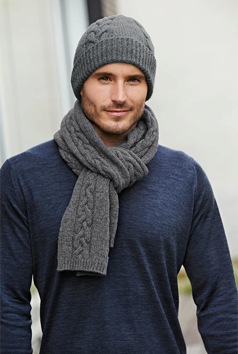 Homme portant un bonnet en tricot torsadé gris et une écharpe, vêtu d'un pull bleu.