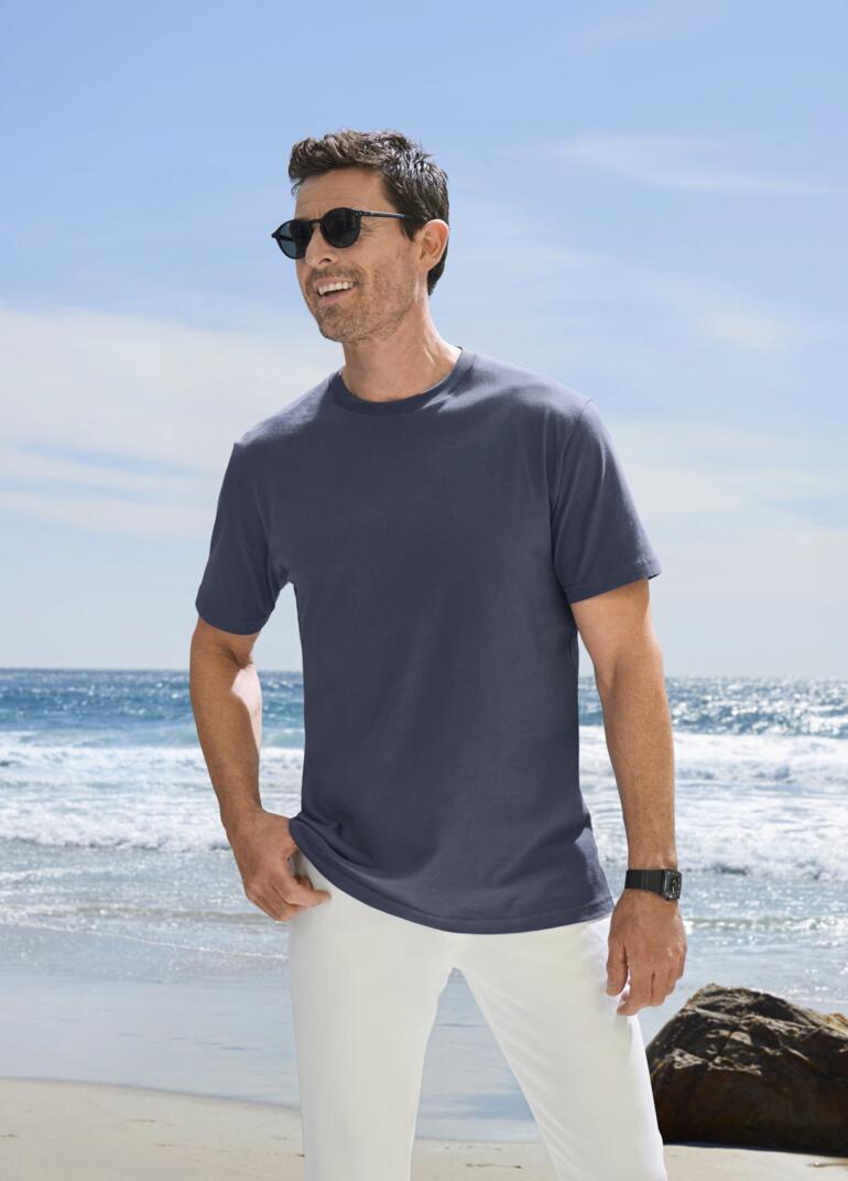 Homme avec un T-shirt bleu et des lunettes de soleil à la plage.
