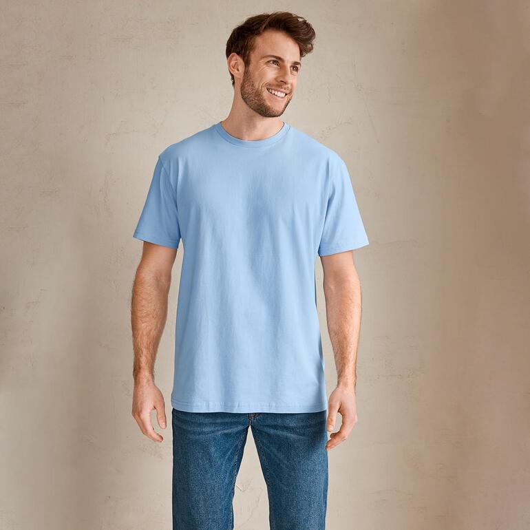 Homme en T-shirt bleu clair souriant devant un fond neutre.