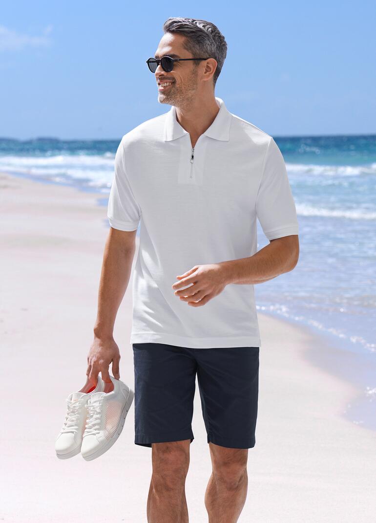 Homme en polo blanc et shorts noirs sur la plage.