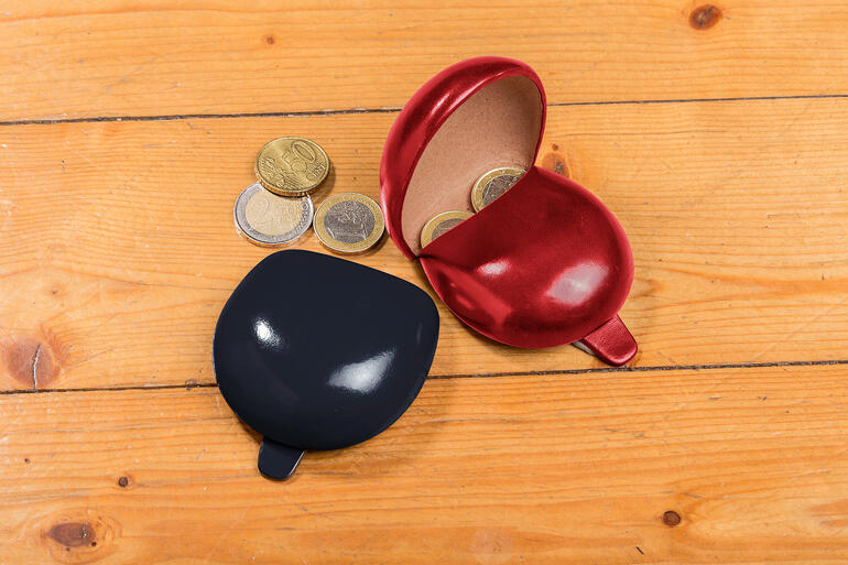 Porte-monnaie rouge et noir avec un rabat ouvert et des pièces sur une table en bois.