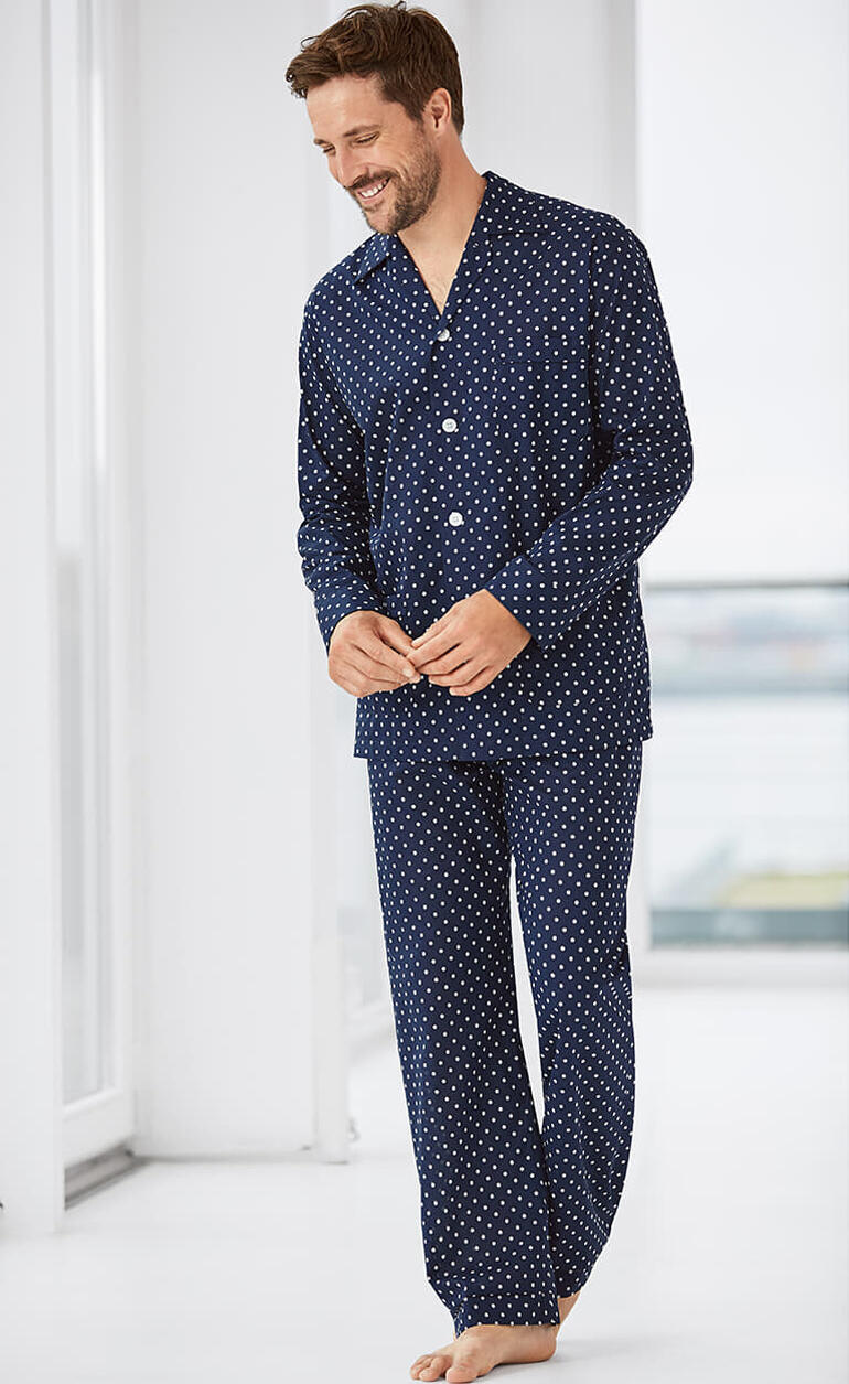 Homme en pyjama bleu marine à pois blancs, souriant dans la pièce.