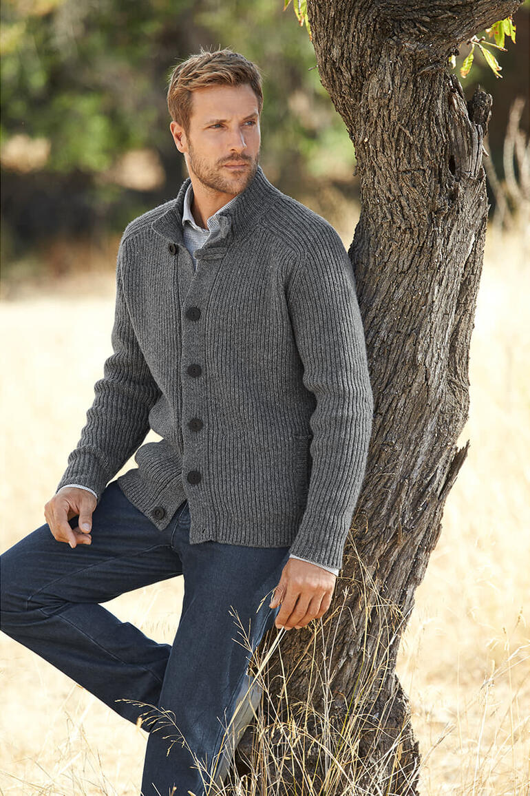 Gris Homme en cardigan Fisherman gris adossé à un arbre.