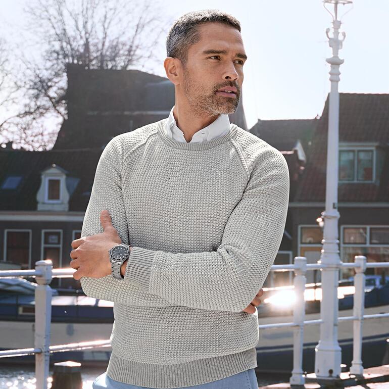 Homme regardant pensivement dans un pull en tricot à motif Carbery gris.