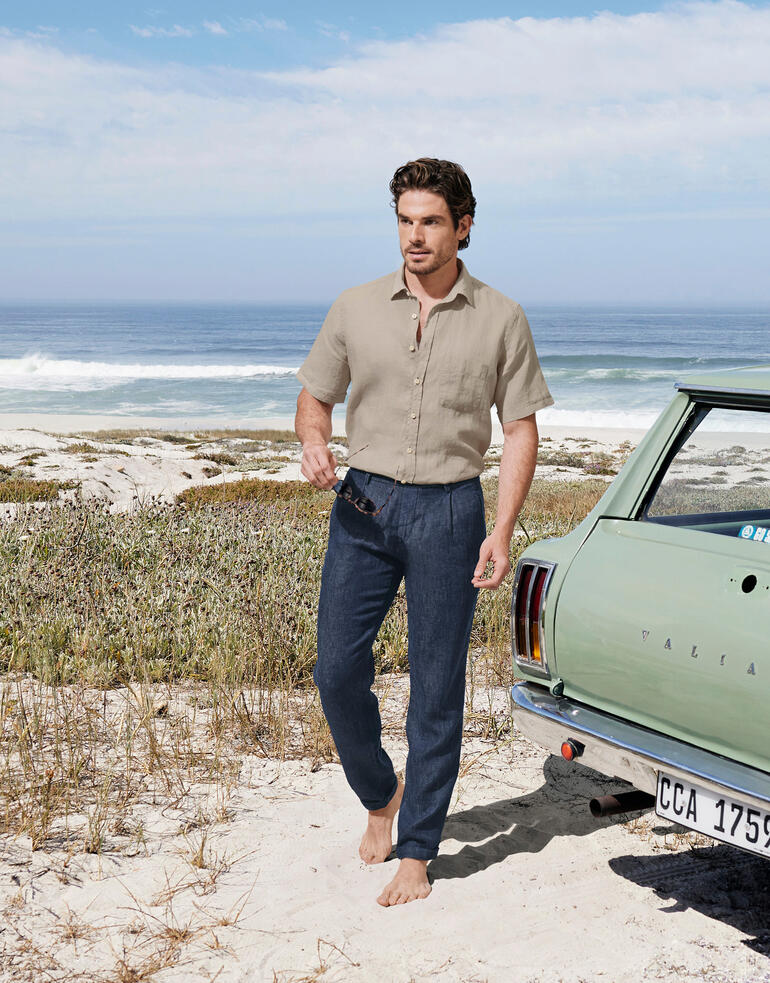 Pantalon en lin g1920 Homme en veste en cuir et pantalon en lin indigo sur la plage devant une voiture.