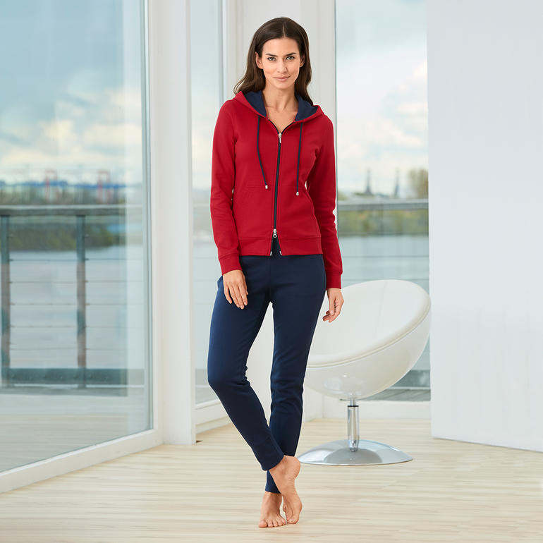 Femme en homesuit en coton Pima rouge et pantalon bleu se tient dans une pièce lumineuse