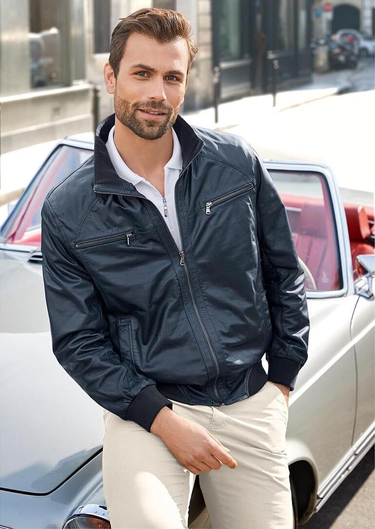 Homme posant dans une blouson d'été en cuir bleu devant une voiture.