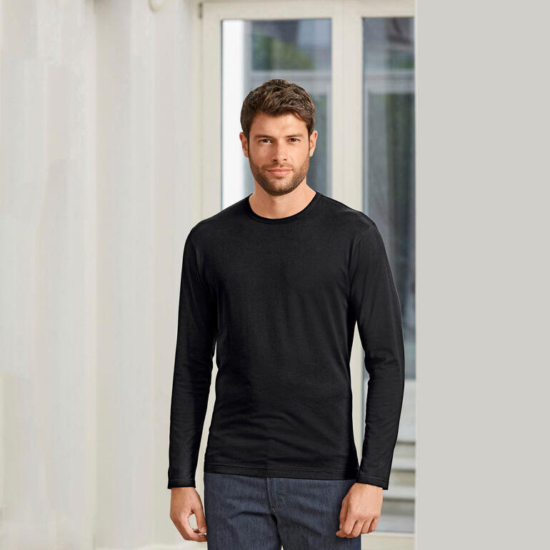 Homme portant un t-shirt Sunspel noir, debout dans une pièce avec des fenêtres lumineuses.