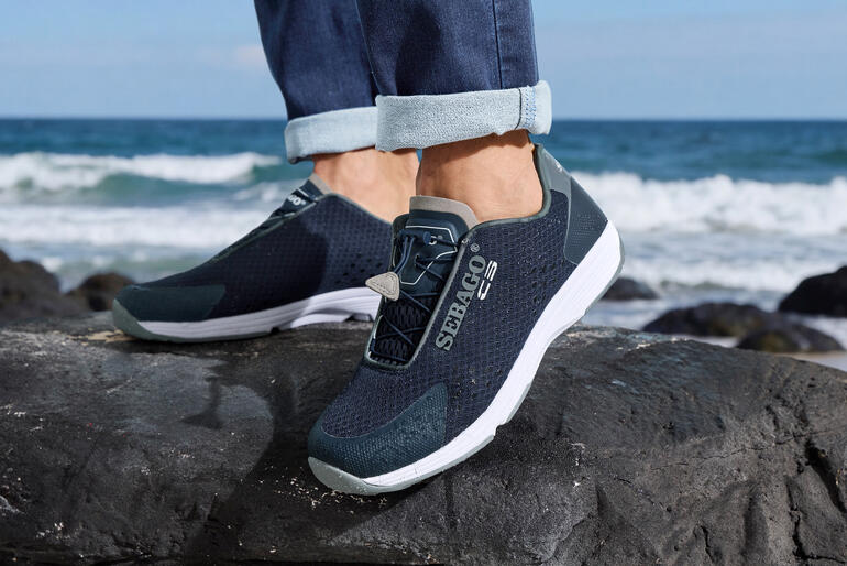 Sneakers Wet pour hommes Sebago en marine, portés sur une plage avec des vagues en arrière-plan.