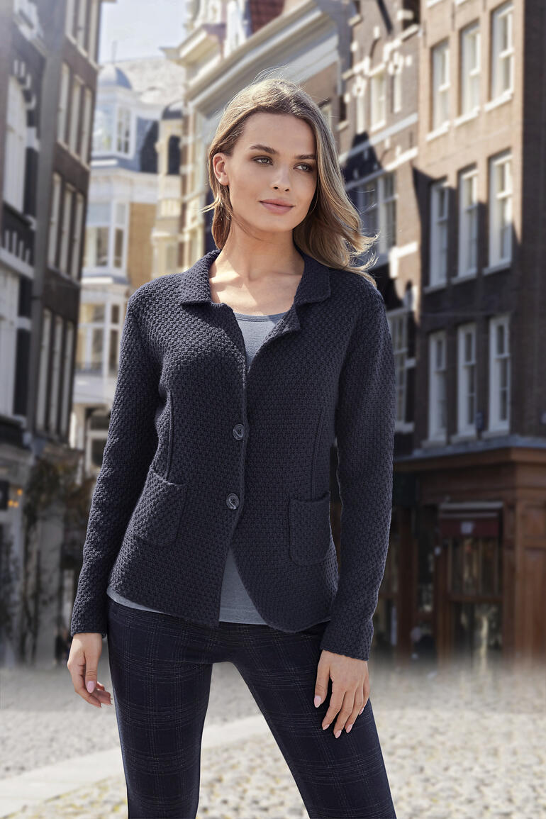 Femme en blazer se tenant devant un décor urbain pittoresque.