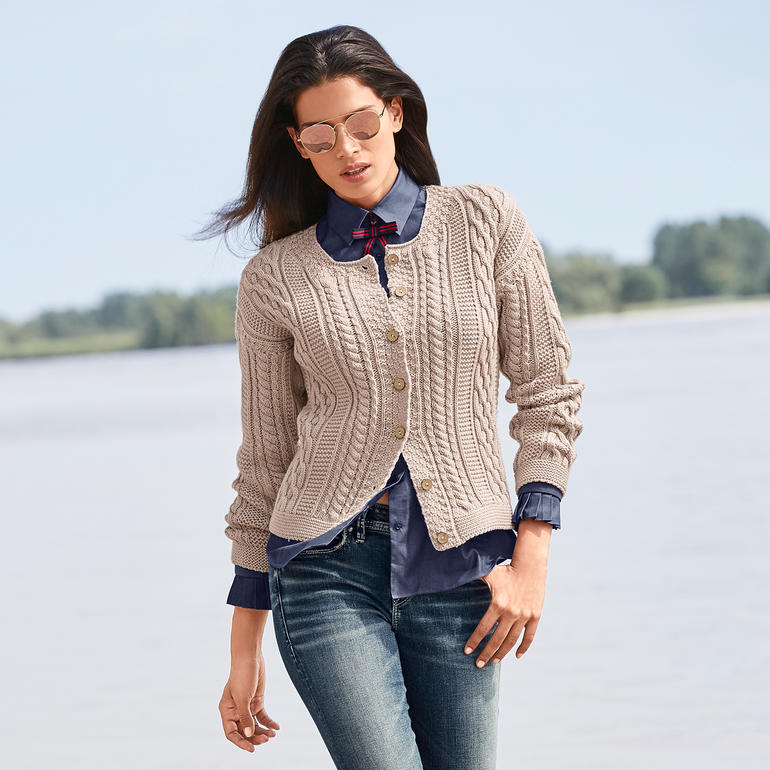Cardigan en tricot Aran Peregrine pour femme Cardigan pour femme beige, avec un motif en relief et des boutons, porté par une femme sur la plage.