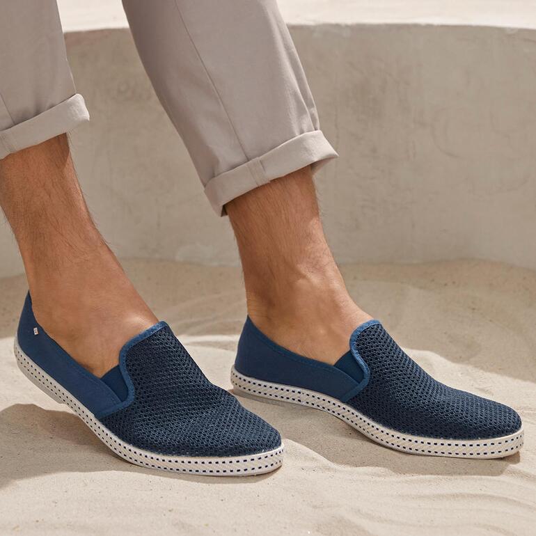 Homme portant des slippers d'été Rivieras bleu marine, debout sur du sable.
