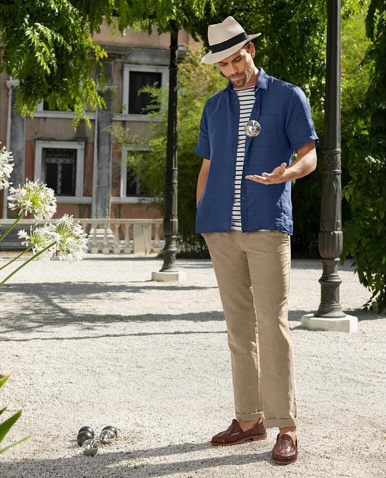 Homme en chemise vintage en lin bleu Dorani, debout dans un paysage de jardin.