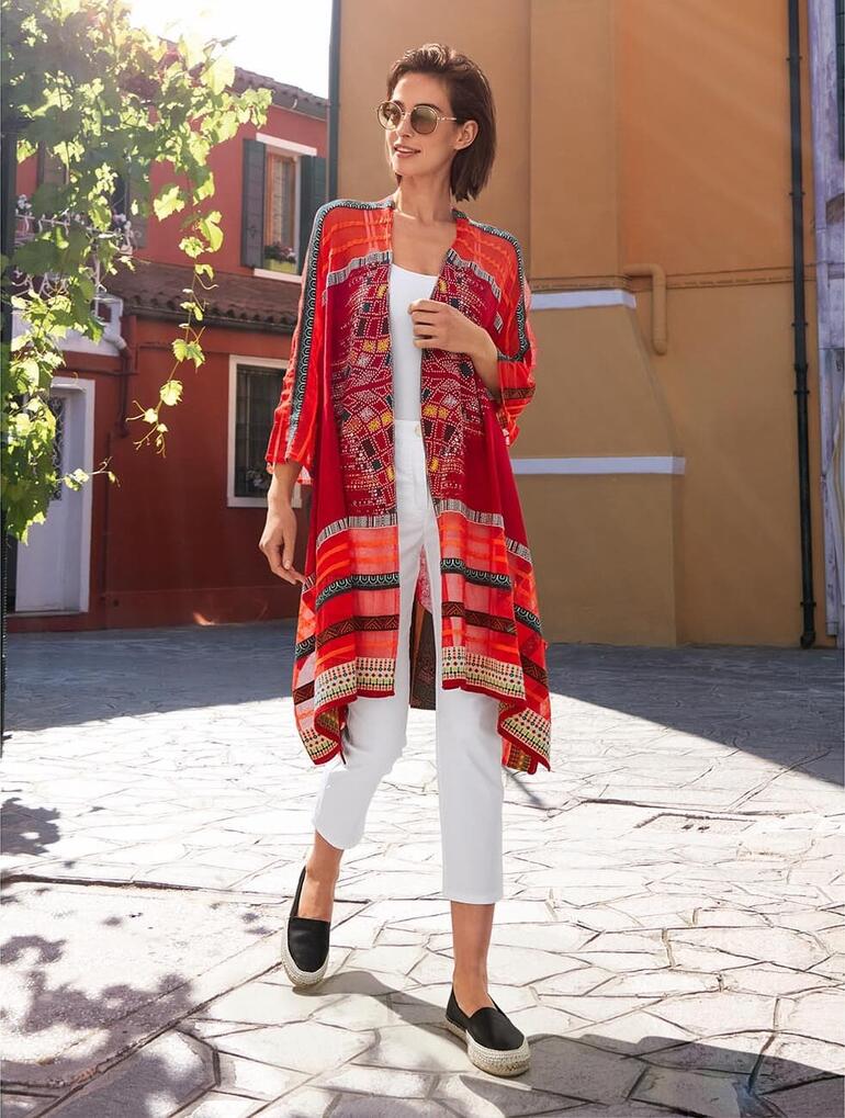 Femme en rouge avec un cardigan IVKO, marche sur une place pavée