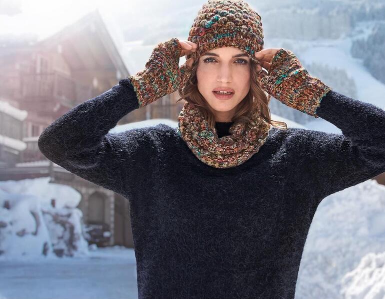 Femme avec un bonnet coloré et des gants dans un paysage enneigé.