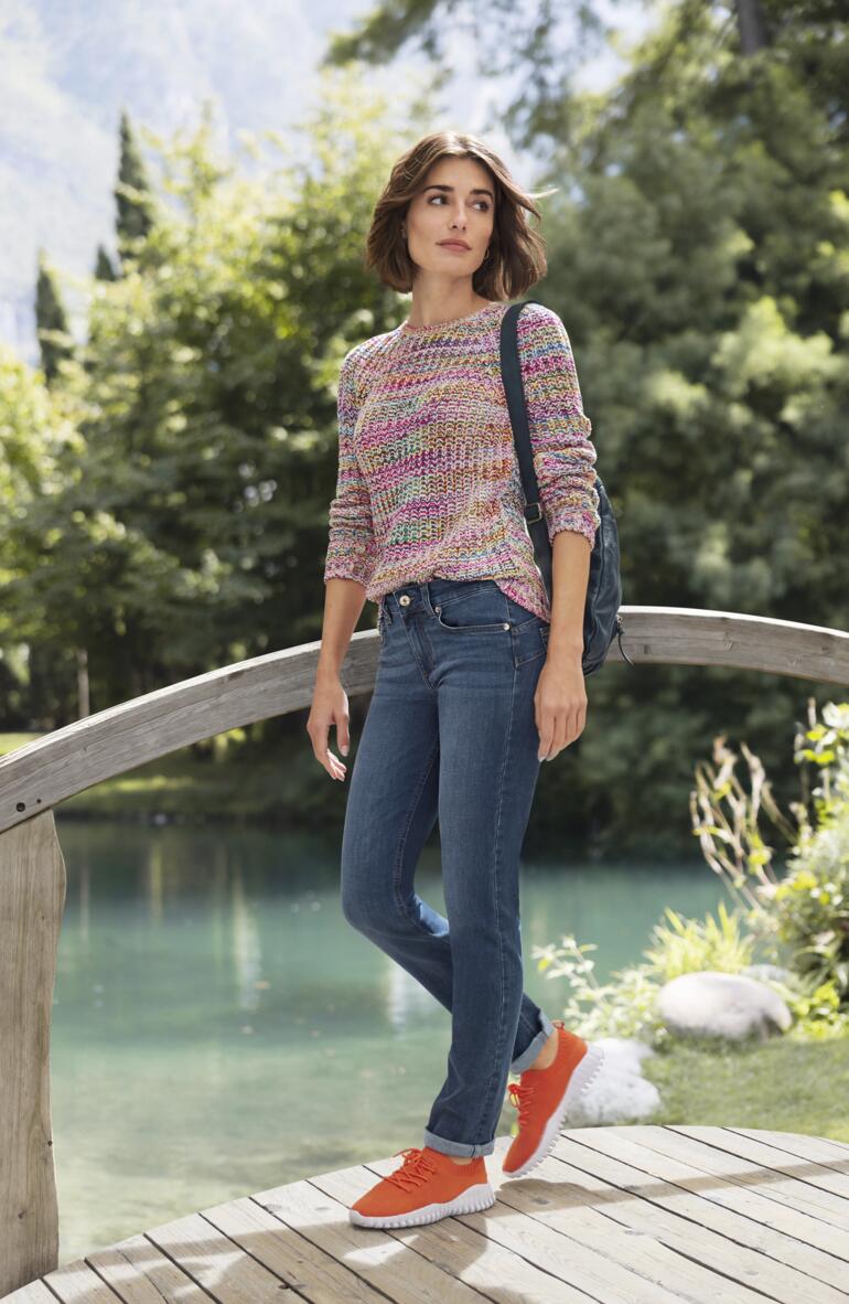 Femme portant un pull en coton multicolore sur un pont en bois dans un paysage idyllique.