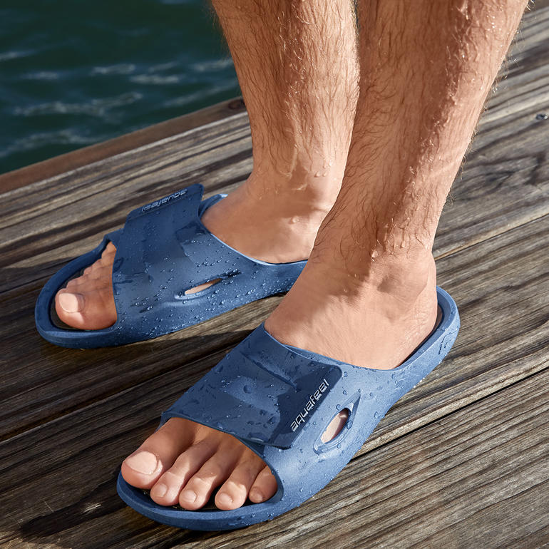 Pieds dans des sandales bleues sur une terrasse en bois au bord de l'eau.