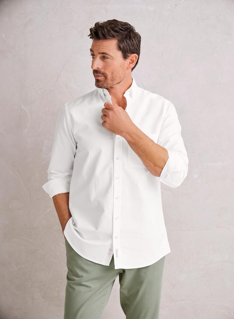 Homme en chemise blanche avec arrière-plan vert se tient pensif.