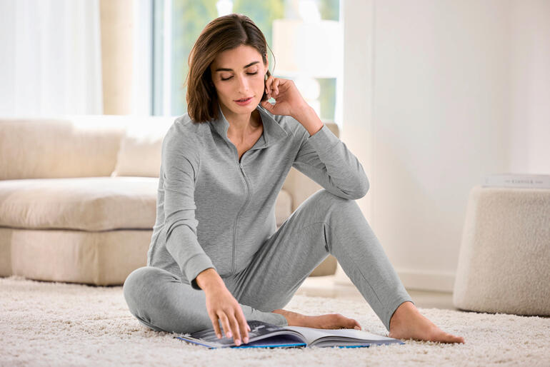 Femme assise en ensemble modal gris en train de lire un livre.