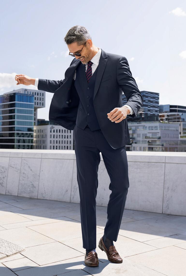 Homme en costume bleu saute joyeusement sur un toit avec vue sur la ville.